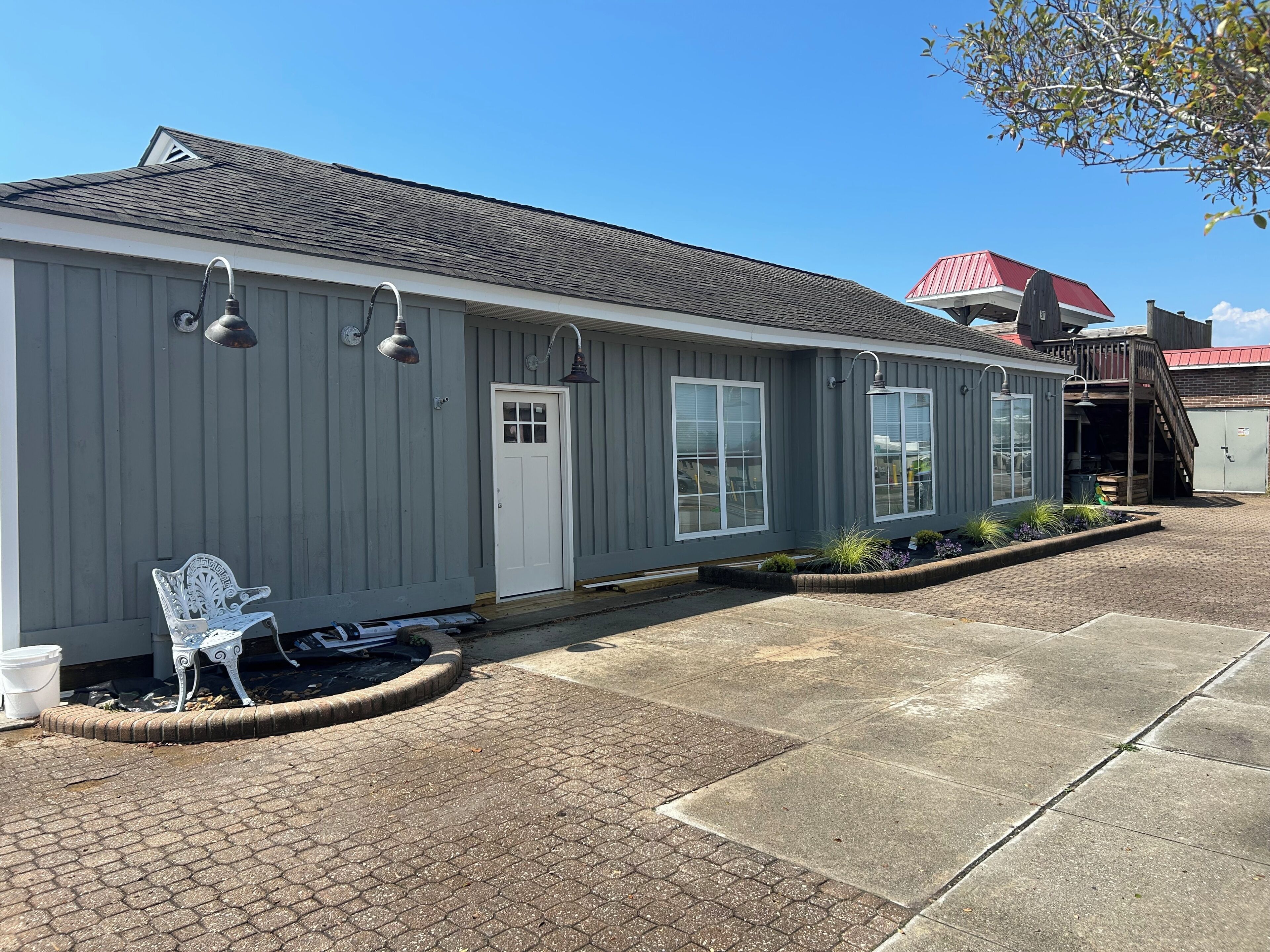 A single-story building with a grey exterior, a white door, and a small porch area with a bench.