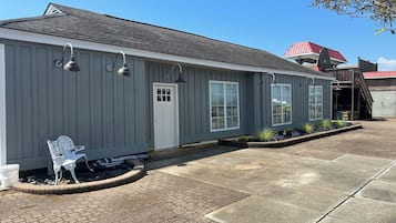 A single-story building with a grey exterior, a white door, and a small porch area with a bench.