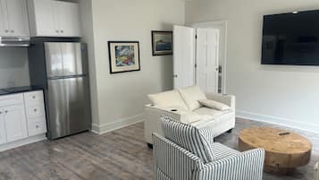 A modern kitchen with stainless steel appliances, a dining area with a striped chair, and a flat-screen TV mounted on the wall.