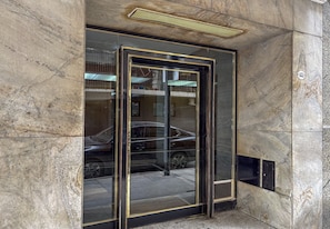 A building entrance with a glass door and a metal frame, a car parked outside, and a sign with the number '1451' on the wall. - Studio Central Located in Recoleta | Av. Santa Fe, universities & health centers (Buenos Aires)