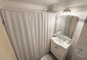 A bathroom with a shower curtain, a sink with a mirror, and a towel rack. - Studio Central Located in Recoleta | Av. Santa Fe, universities & health centers (Buenos Aires)