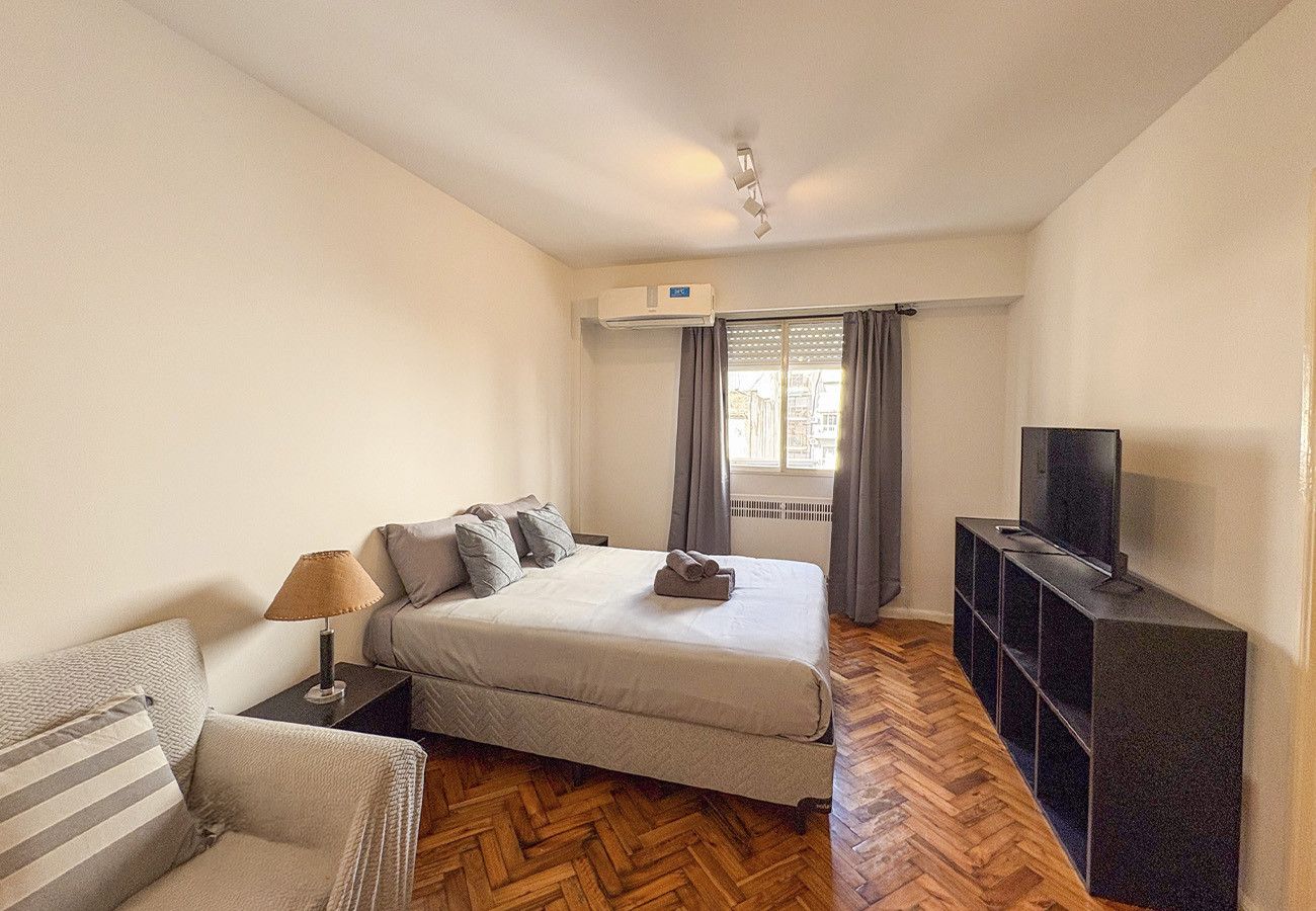 A bedroom with a bed, a TV stand, a sofa, and a window with curtains.