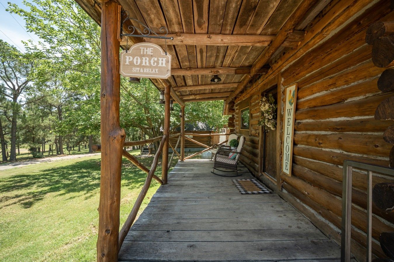 A wooden porch with a sign reading 'The Porch Sit & Relax' and a 'Welcome' sign on the wall.