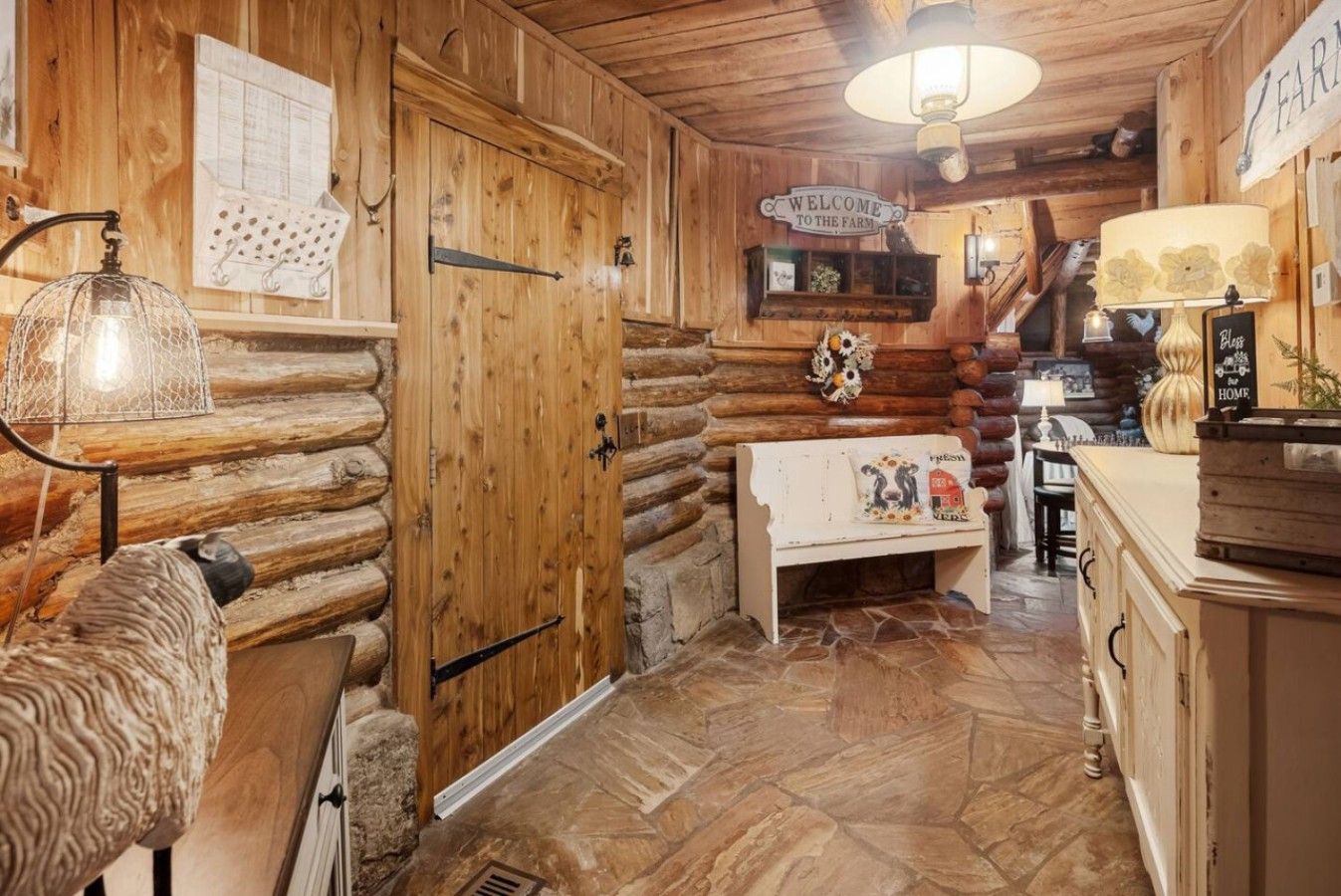 A rustic wooden interior with a bench, a welcome sign, and a lamp.