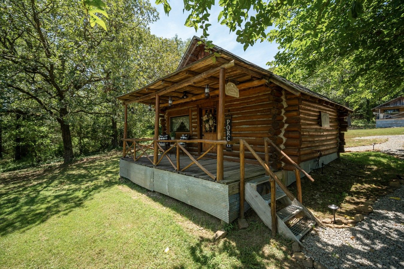 A rustic log cabin with a porch, surrounded by trees.