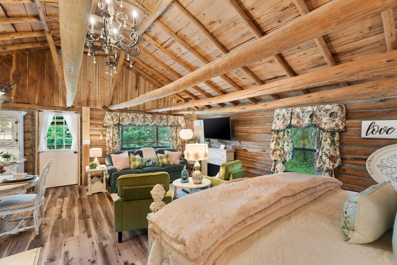 A rustic cabin interior with a wooden ceiling, a sofa set, a television, and a 'love' sign on the wall.