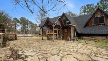 A rustic cabin with a stone patio, wooden exterior, and a covered entryway.