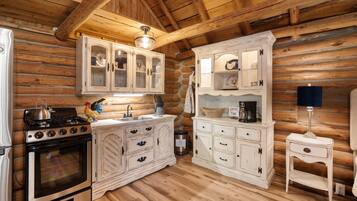 A rustic kitchen with wooden walls, a stove, cabinets, and a coffee maker.