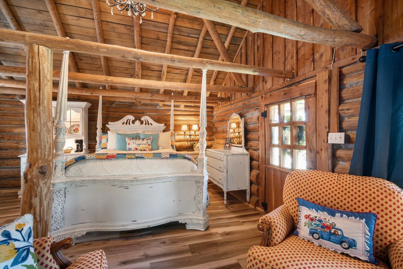 A rustic log cabin interior with a four-poster bed, a dresser, and a patterned armchair.