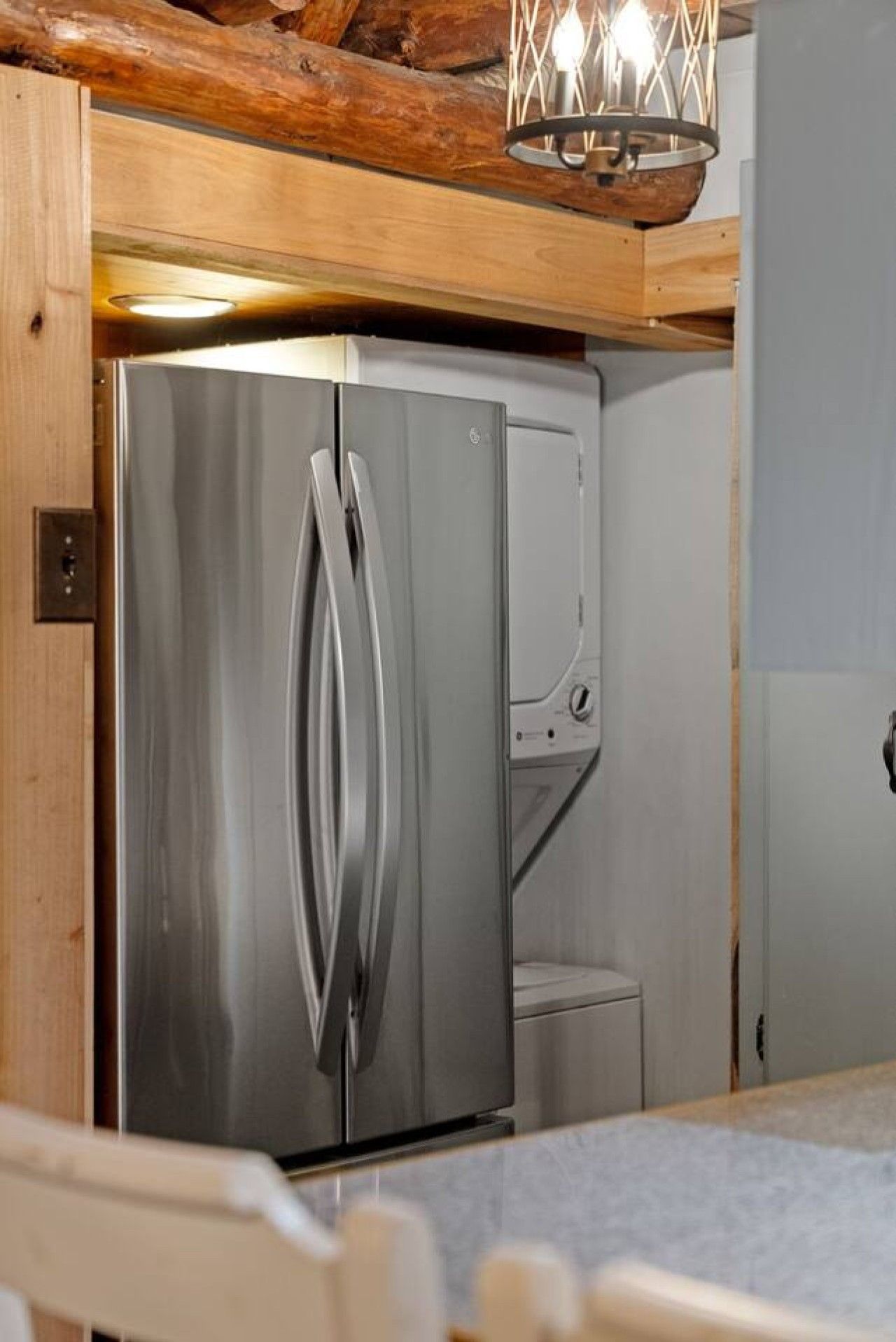 A stainless steel refrigerator with a freezer compartment, located in a kitchen with wooden ceiling beams and a pendant light fixture.