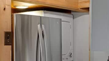 A stainless steel refrigerator with a freezer compartment, located in a kitchen with wooden ceiling beams and a pendant light fixture.