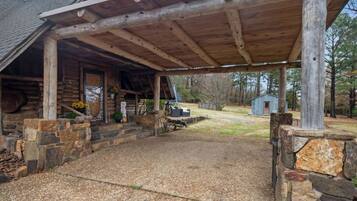 A covered porch with stone walls, a gravel driveway, and a small shed in the background.