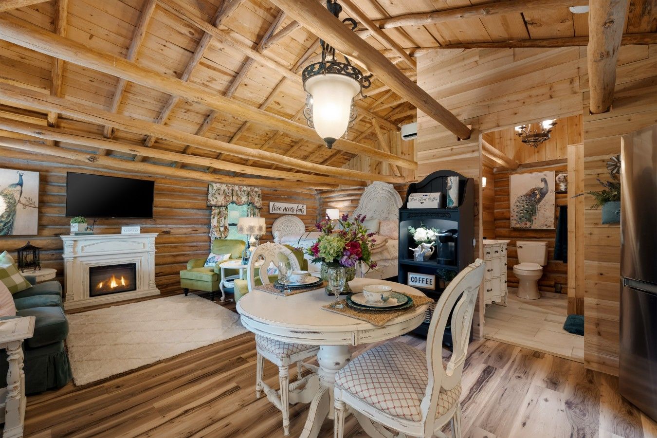 A log cabin interior with a fireplace, dining table, chairs, a television, and a coffee station.