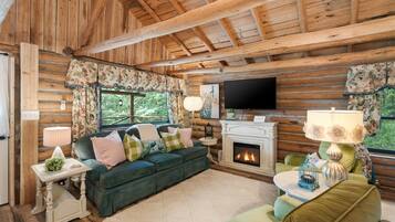 Interior de una cabaña de madera con chimenea, televisor y sofá.