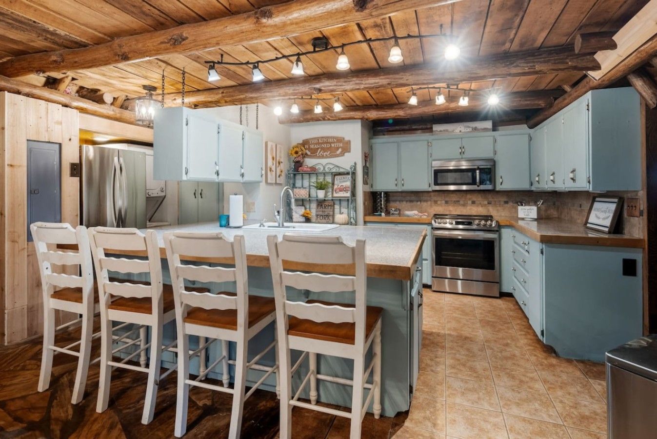 A kitchen with a central island, wooden chairs, and a stainless steel refrigerator.