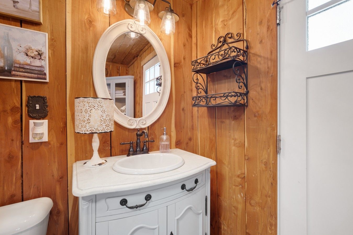 A bathroom with a wooden wall, a round mirror, a white sink, and a small shelf.
