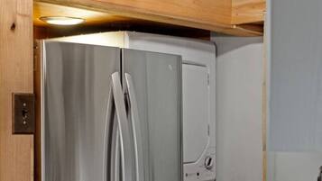 A stainless steel refrigerator with a freezer compartment, located in a kitchen with wooden ceiling beams and a pendant light fixture.