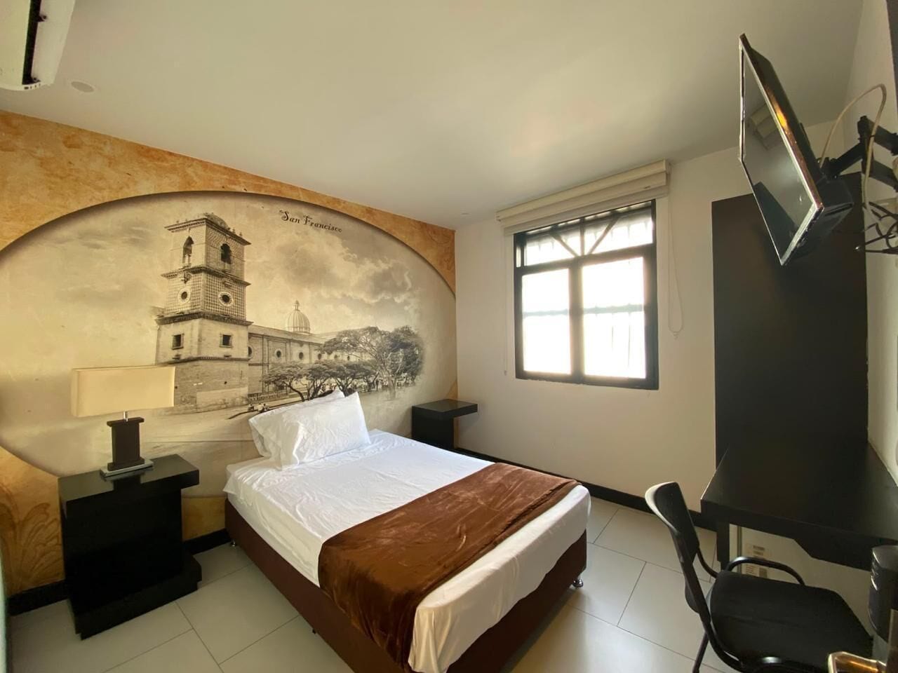 A hotel room with a bed, a desk, a chair, a TV, and a window.