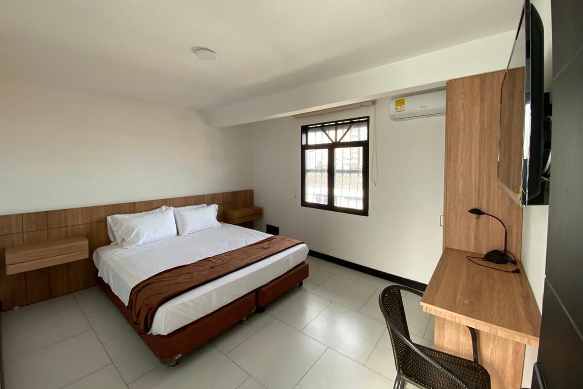 A hotel room with a bed, a desk, a chair, a TV, and a window.