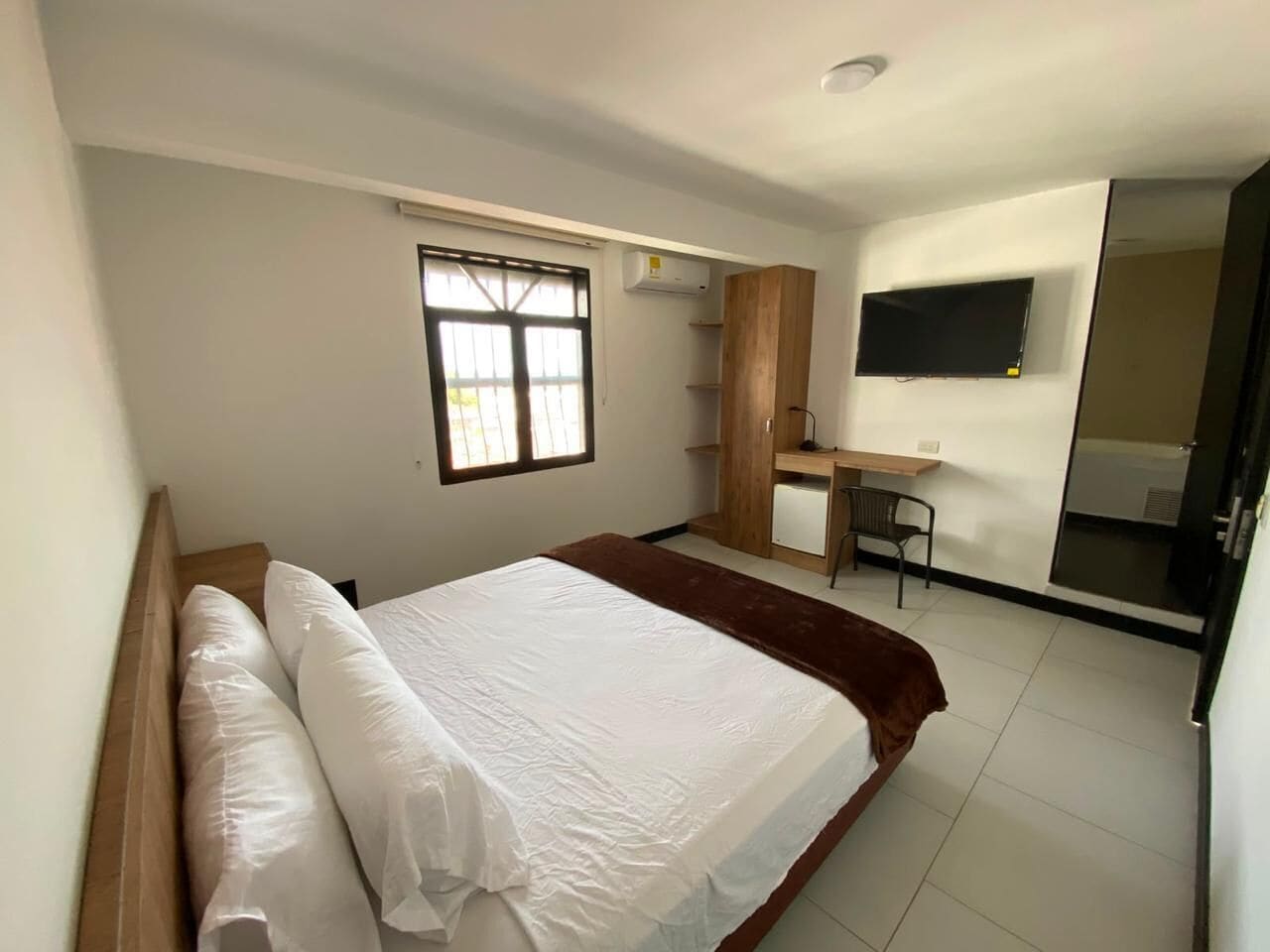 A bedroom with a bed, a desk, a chair, and a TV.