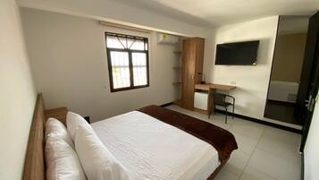 A bedroom with a bed, a desk, a chair, and a TV.