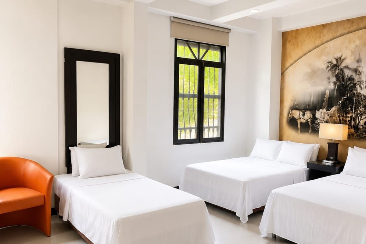 A hotel room with two beds, a chair, a painting, and a window with a view.