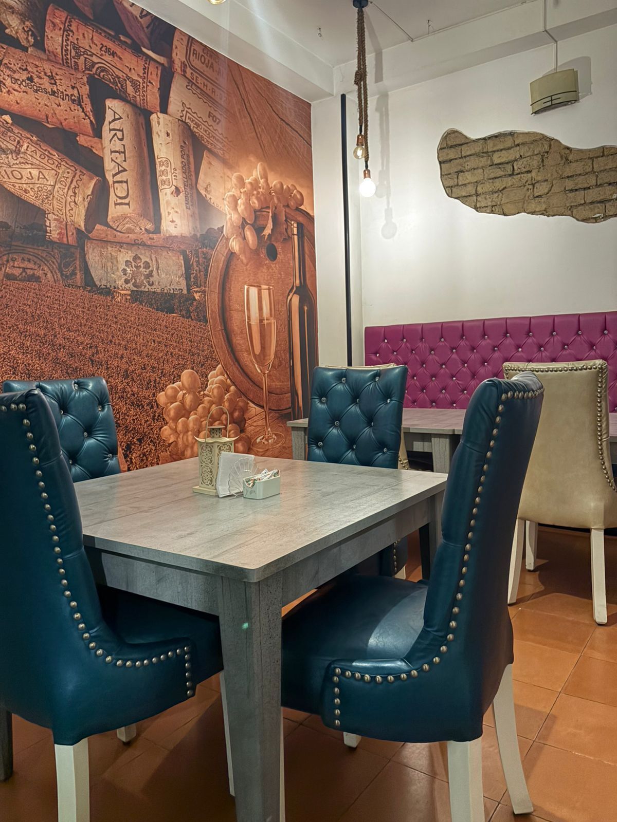 A dining area with a long table, four upholstered chairs, a wall mural, and a brick accent wall.