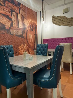 A dining area with a long table, four upholstered chairs, a wall mural, and a brick accent wall.