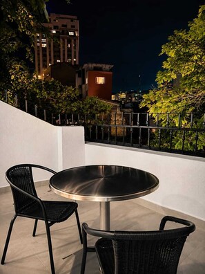 Una terrazza esterna con un tavolo rotondo e due sedie, circondata da un muro bianco e una ringhiera in metallo.