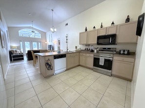 A modern kitchen with a central island, stainless steel appliances, and light-colored cabinetry. - Tropical Golf Paradise (Haines City)