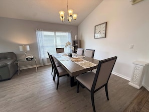 A dining area with a wooden table, chairs, a chandelier, and a clock on the wall. - Tropical Golf Paradise (Haines City)
