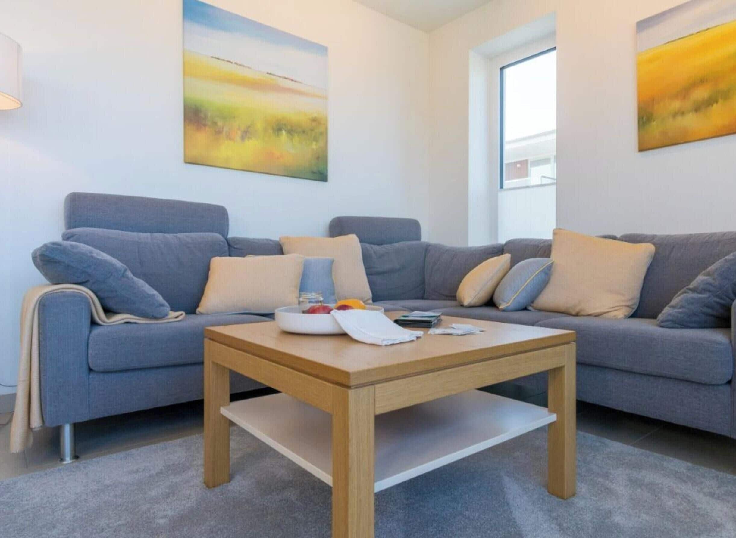 A modern living room with a grey sofa, a wooden coffee table, and two paintings on the walls.