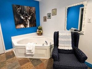 A bathroom with a large bathtub, a chair, a mirror, and wall art.