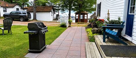 A pathway leading to a house with a barbecue grill, a bench, and a small shed.