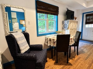 A room with a dining table, chairs, a large mirror, and a window with a view of greenery.