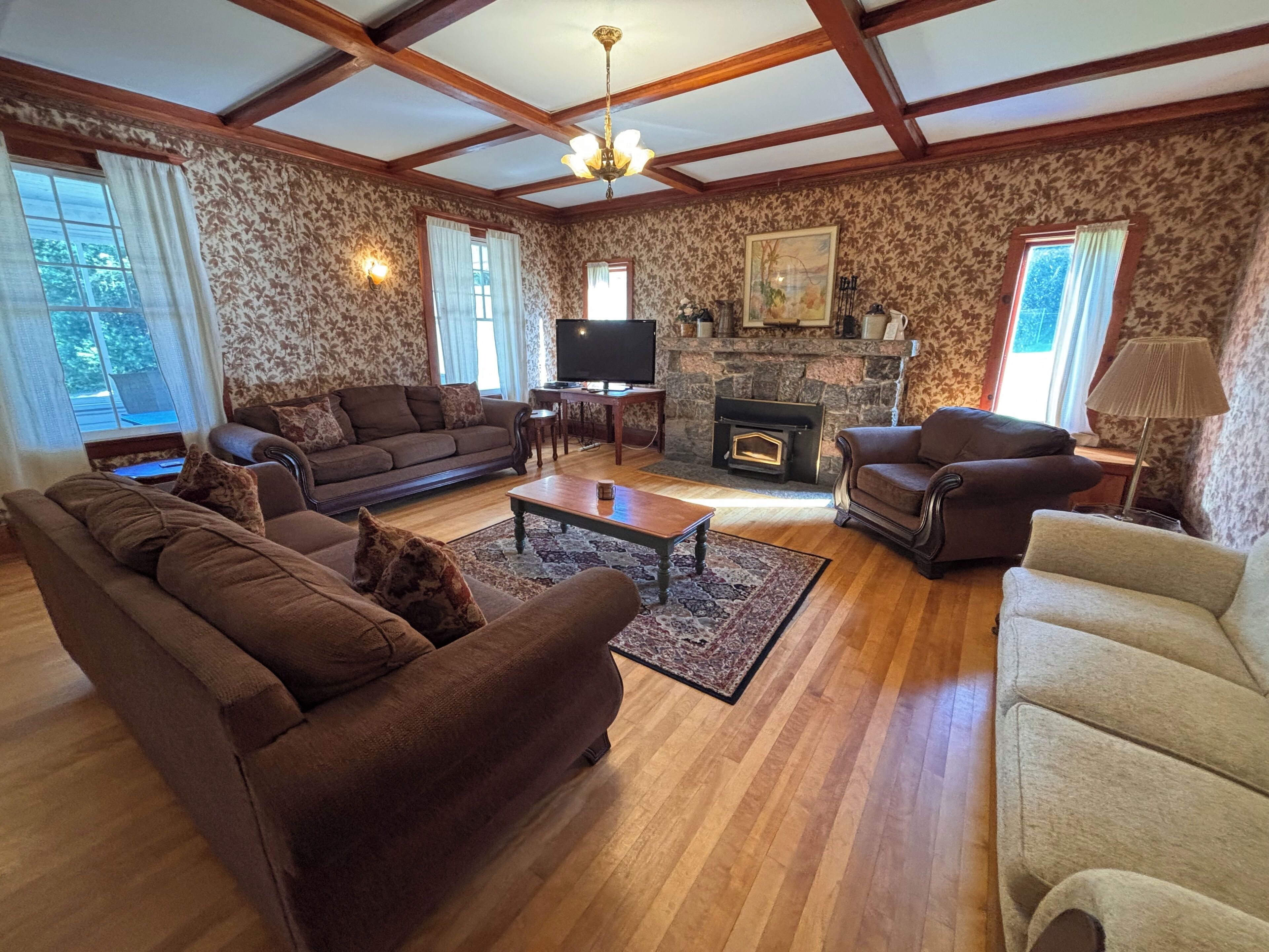 A living room with a fireplace, wooden floors, and patterned wallpaper.