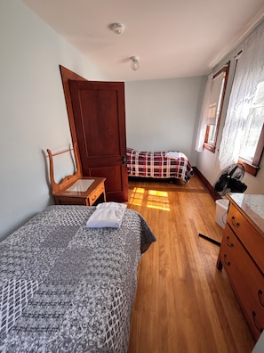 A bedroom with two beds, a wooden dresser, a small table, and a window with curtains. - Main Cottage of historic Muskoka resort Clyffe House.  Very spacious 5 bedroom (Port Sydney)