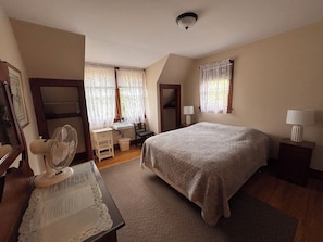 Una camera da letto con un letto, lampade sui comodini, una scrivania con una sedia, uno specchio e una ventola.