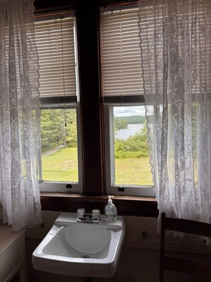 Un bagno con un lavandino, due finestre con persiane e vista su un paesaggio verde.