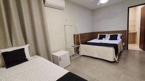 Ein Hotelzimmer mit zwei Betten, einem kleinen weißen Schrank, einem Wäscheständer und einer Tür zu einem Badezimmer.