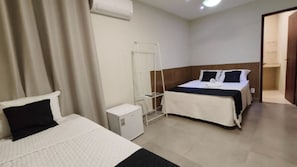 Une chambre d’hôtel avec deux lits, une petite armoire blanche, un étendoir et une porte donnant sur une salle de bain.