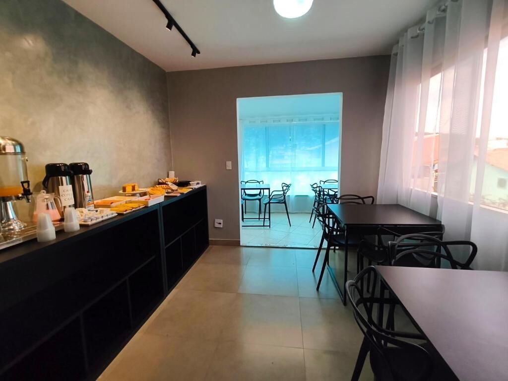 A modern kitchen with a long counter, a coffee station, and a view through a glass door to an outdoor seating area.