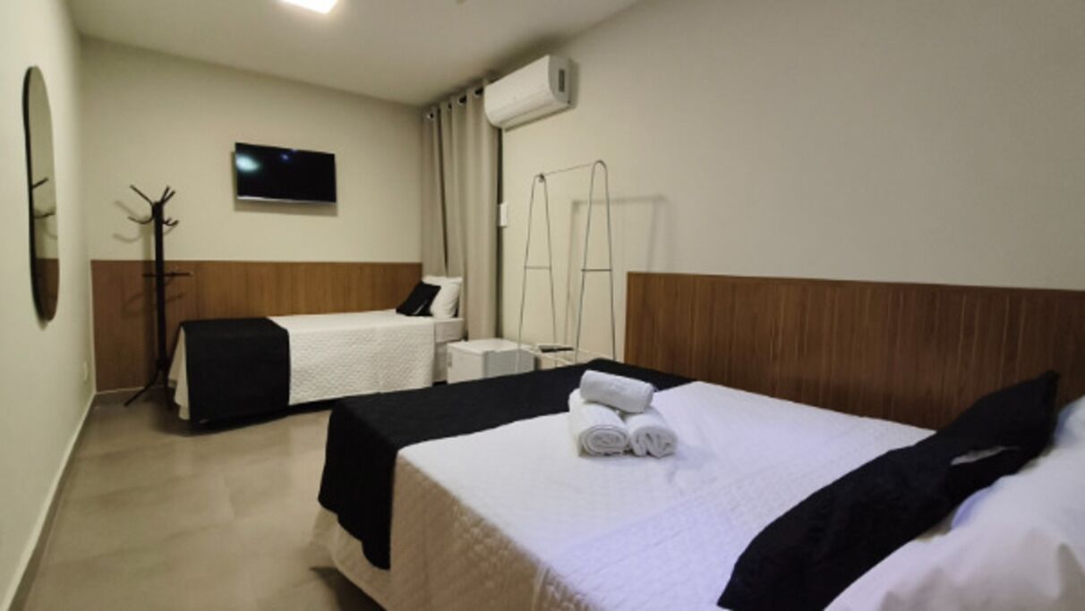 A hotel room with two beds, a TV, a coat rack, and a window with curtains.