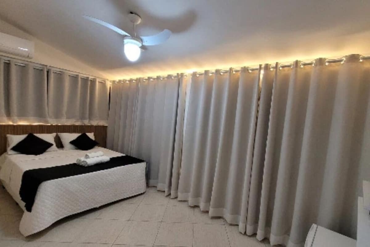 Une chambre d’hôtel équipée d’un lit, de rideaux, d’un ventilateur de plafond et d’un téléviseur à écran plat.