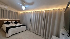 Habitació d'hotel amb llit, cortines, ventilador de sostre i televisió de pantalla plana.