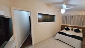 Un dormitorio con cama, ventilador de techo, ventana con persianas y una puerta.