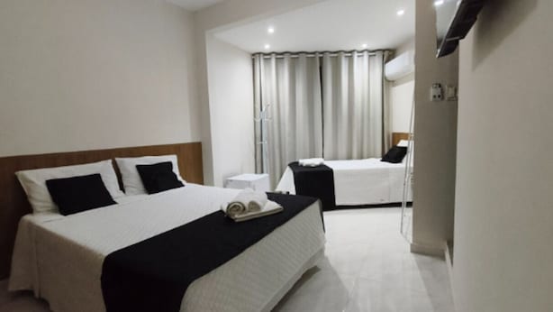Ein Hotelzimmer mit zwei Betten, einem Nachttisch, einer Lampe und einem Fenster mit Vorhängen.