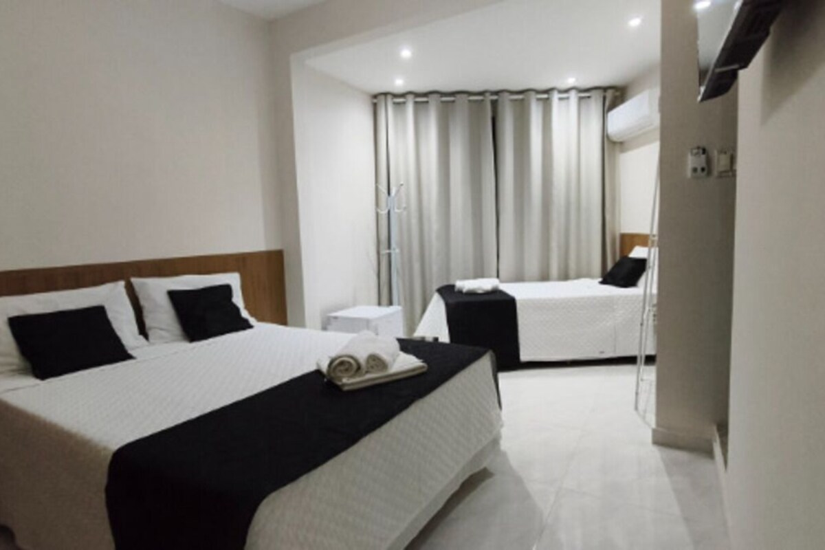 Une chambre d’hôtel avec deux lits, une table de chevet, une lampe et une fenêtre avec des rideaux.