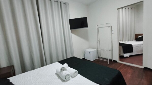 Une chambre d’hôtel avec un lit, un téléviseur fixé au mur, une petite table de chevet et un miroir qui reflète la pièce.