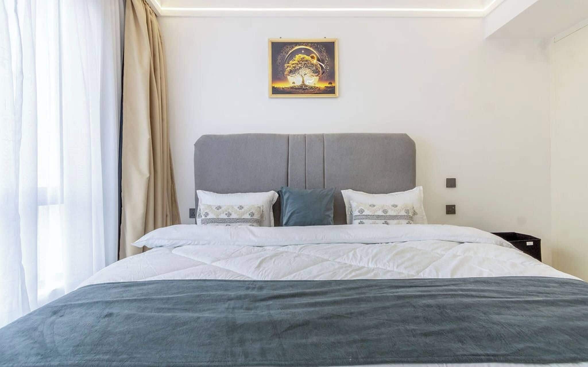 Habitación de hotel con cama, cortinas, un cuadro en la pared y una mesita de noche.